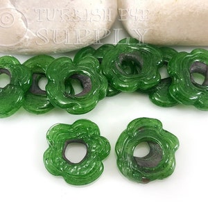 May include: Green glass flower-shaped beads with a hole in the center. The beads have a textured surface and are approximately 1 inch in diameter.