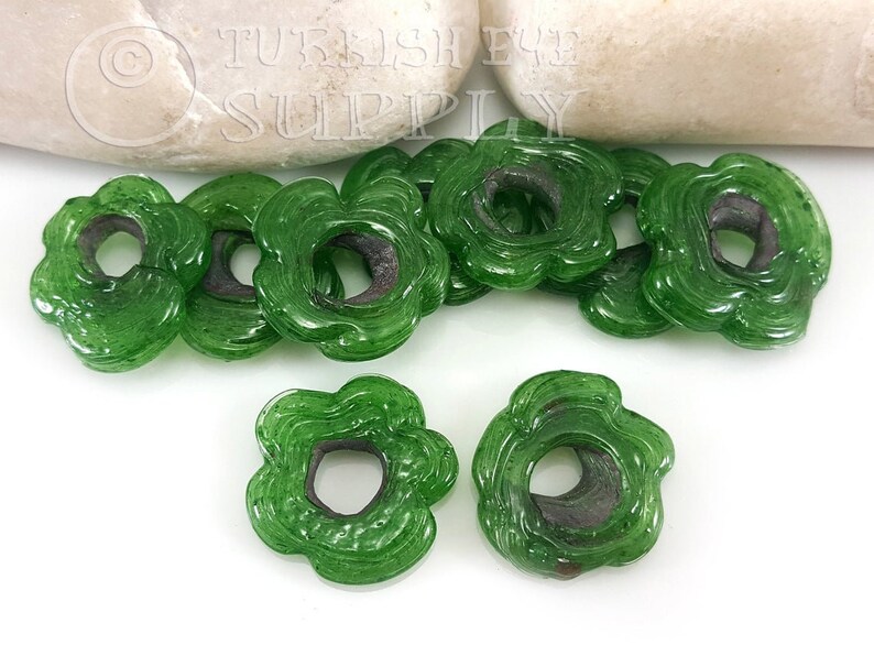 May include: Green glass flower-shaped beads with a hole in the center. The beads have a textured surface and are approximately 1 inch in diameter.