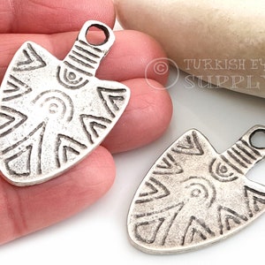 May include: Two silver-toned arrowhead-shaped pendants with intricate geometric designs. The pendants have a loop at the top for attaching to a chain or cord.