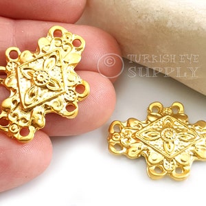 Può includere: Due ciondoli connettore in metallo dorato con intricati disegni floreali e quattro fori per attaccare gioielli. I ciondoli hanno la forma di un diamante con un centro rialzato.