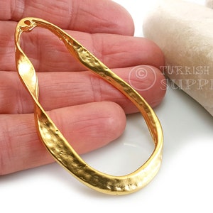 May include: A gold-toned twisted oval ring with a hammered finish. The ring is open and has a hole at the top for attaching a pendant or charm.