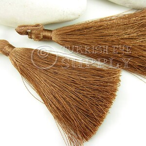May include: Two brown silk tassels with a long fringe. The tassels are tied together with a thin cord.