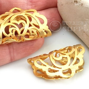Puede incluir: Dos tapones de extremo de filigrana de metal de color dorado para la elaboración de joyas. Los tapones tienen forma de semicírculo y presentan un diseño delicado e intrincado.