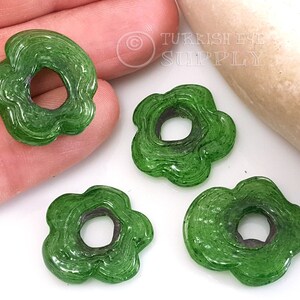 May include: Four green glass flower-shaped beads with a hole in the center. The beads have a textured, swirled design.