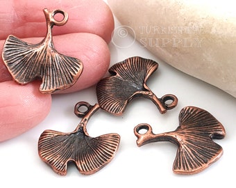 May include: Four antique copper-toned ginkgo leaf charms with a loop for hanging. The leaves have a detailed, textured design.