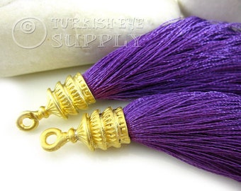 May include: Two purple silk tassels with gold metal tips. The tassels are approximately 3 inches long and have a decorative, ornate design.