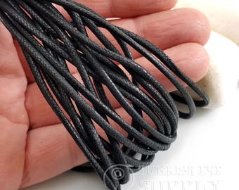 May include: Close-up of a bundle of black waxed cotton cord. The cord is tightly woven and appears to be durable. The cords are held in a hand, with a white background.