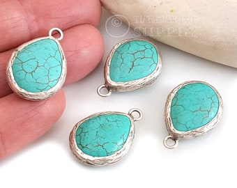 Op de afbeelding: Vier turquoise druppelvormige hangers met een zilverkleurige, getextureerde rand. De turkoois steen heeft een gebarsten patroon. Elke hanger heeft een kleine lus aan de bovenkant om aan een ketting of ander sieradenonderdeel te bevestigen.