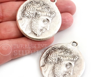 May include: Two silver-toned metal pendants featuring a profile of a man with a beard and a crown. The pendants have a loop at the top for attaching to a chain or cord.