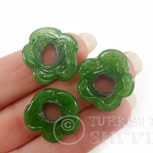 May include: Three green glass flower-shaped beads with a hole in the center. The beads have a swirl pattern and a translucent finish.