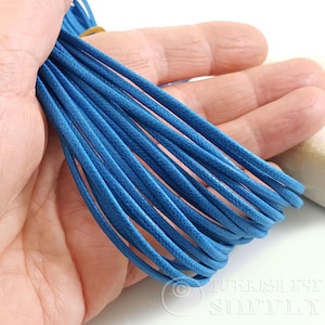 May include: A bundle of bright blue waxed cotton cord held in a hand. The cord appears to be tightly wound and ready for use in jewelry making or other crafts. The color is a vibrant, solid blue.