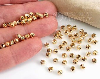 May include: A close-up of a pile of gold-colored metal beads. The beads are round and have a textured surface. The beads are about 6mm in diameter.