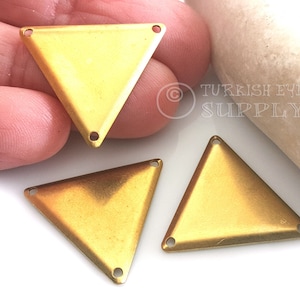 Puede incluir: Tres abalorios de metal de forma triangular de color dorado con agujeros en cada esquina. Los abalorios están sobre una superficie blanca.