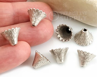 May include: Seven silver metal cone-shaped beads with scalloped edges. The beads have a textured surface and a hole at the top for stringing.