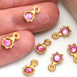 Pode incluir: Encantos de metal dourado com um strass rosa no centro e um laço na parte superior. Os encantos são perfeitos para fazer joias ou adicionar um toque de brilho a trabalhos manuais.