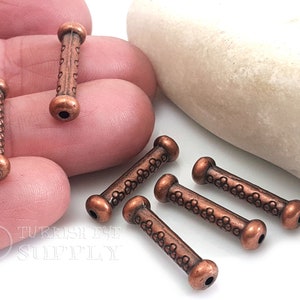 Puede incluir: Seis cuentas de metal de color cobre con un patrón decorativo. Las cuentas son cilíndricas con extremos redondeados. Las cuentas miden aproximadamente 2,5 cm de largo.