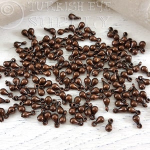 May include: A large quantity of small, teardrop-shaped metal charms with a loop at the top. The charms are a copper color.