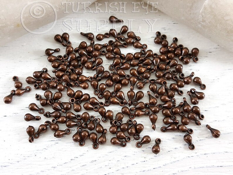 May include: A large quantity of small, teardrop-shaped metal charms with a loop at the top. The charms are a copper color.