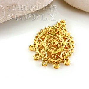 May include: Gold-toned metal pendant with a circular filigree design and four hanging loops. Turkish Eye Supply is printed on the background.