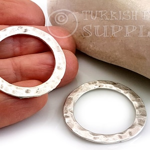 Puede incluir: Dos anillos de metal plateados con textura martillada. Los anillos son redondos y tienen un borde interior liso.