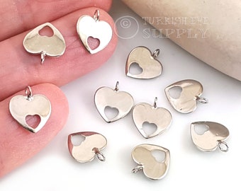 May include: A collection of silver-toned metal heart charms with a smaller heart cut-out in the centre. Each charm has a loop at the top for attaching to jewellery or other crafts.
