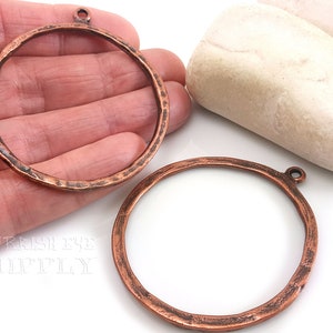 Könnte beinhalten: Zwei kupferfarbene Metallringe mit gehämmerter Textur und einem Sprungring oben. Die Ringe haben einen Durchmesser von etwa 5 cm.