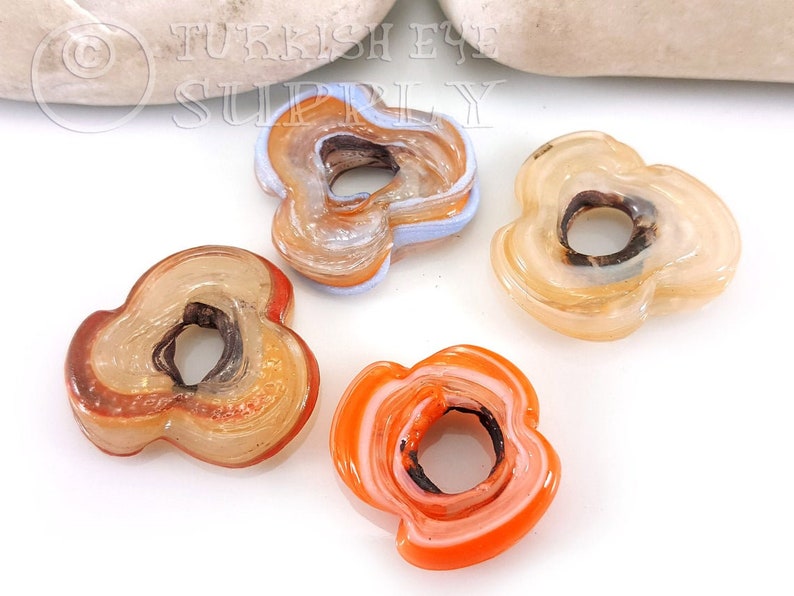 May include: Four agate flower-shaped beads with a hole in the center. The beads are in shades of orange, brown, and white.