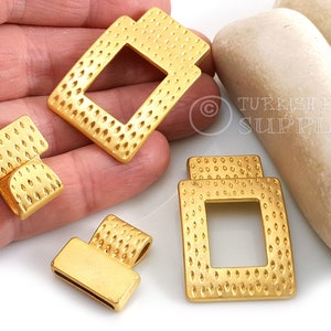 Puede incluir: Cuatro piezas de conexión de metal dorado con una superficie texturizada y forma cuadrada. Cada pieza tiene una abertura cuadrada en el centro.
