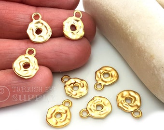 May include: Seven gold-toned metal charms with a textured, hammered finish. Each charm has a round shape with a hole in the center and a small loop at the top for attaching to jewelry.