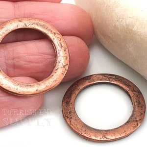 May include: Two copper rings with a distressed finish. The rings are about 1 inch in diameter and have a smooth, rounded edge.