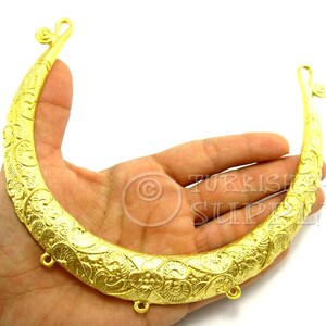 Könnte beinhalten: Eine goldfarbene Halskette aus Metall in Halbmondform mit aufwendigen floralen Mustern. Die Halskette hat vier kleine Schlaufen an der Unterseite.