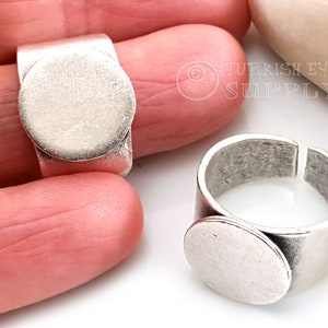May include: Two silver rings with a round, blank, silver bezel. The rings are adjustable and can be used for jewelry making.
