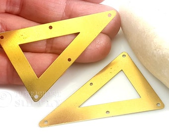 May include: Two gold-colored metal triangle shapes with cut-out centers and holes around the edges.  The triangles are on a white surface.