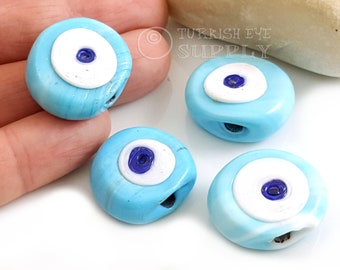 May include: Four blue and white evil eye beads with a hole in the center. The beads are oval shaped and have a white circle with a blue eye in the center.