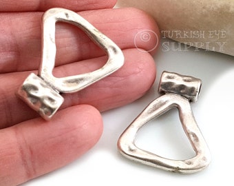 Puede incluir: Dos colgantes de plata en forma de triángulo con textura martillada. Los colgantes tienen un bucle en la parte superior para sujetarlos a un collar o pulsera.