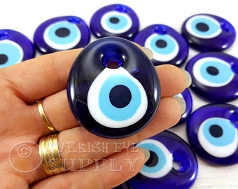 May include: A collection of blue and white evil eye charms, also known as Nazar Boncugu, with a dark blue background. The charms are round and have a white circle with a blue eye in the center.