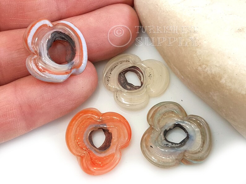 May include: Four agate flower beads with a hole in the center. The beads are in shades of white, orange, and gray.