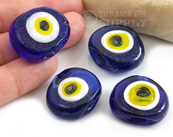 May include: Four blue glass evil eye beads with white and yellow details. The beads are oval shaped and have a hole in the center for stringing.