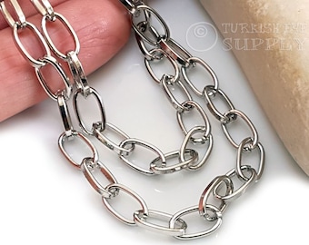 Puede incluir: Primer plano de una brillante cadena plateada con eslabones ovalados. La cadena se muestra sobre una superficie blanca. La cadena probablemente se utiliza para la fabricación de joyas o como elemento decorativo. El texto "TURKISH EYE SUPPLY" es visible en el fondo.