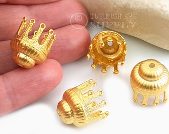May include: Four gold-toned metal bead caps with a crown-like design. The caps have a textured surface and a small hole in the center.