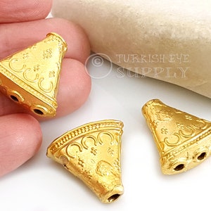 May include: Three gold-toned metal triangle-shaped beads with intricate designs and three holes each.