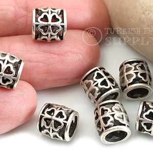 May include: Seven silver-toned metal beads with a four-leaf clover design. The beads are round and have a hole in the centre for threading.