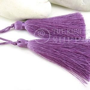 May include: Two purple tassel trims with a loop at the top. The tassels are made of soft, silky threads.