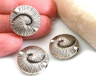 May include: Three silver-toned metal beads shaped like ammonites. Each bead has a spiral design and a hole for stringing.