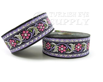 Puede incluir: Un rollo de ribete morado y negro con un diseño floral plateado y flores rosas. El ribete está sobre un fondo blanco.