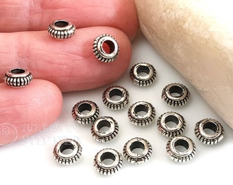 May include: Silver-toned metal spacer beads with a decorative, textured design. The beads are round with a hole in the center. There are 15 beads in total.