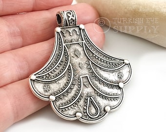 May include: Silver pendant with an intricate, ornate design. The pendant is shaped like a stylized flower with a rounded top and a scalloped bottom. The pendant has a loop at the top for attaching a chain.