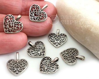 May include: Seven silver filigree heart charms with a delicate, intricate design. Each charm has a loop at the top for attaching to jewellery or other crafts.