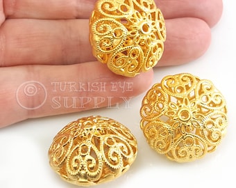 May include: Three gold-colored metal beads with intricate filigree designs. The beads are round and have a hollow center.