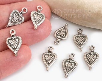 May include: Silver heart-shaped charms with intricate designs. The charms have a loop at the top for attaching to jewellery or other crafts.